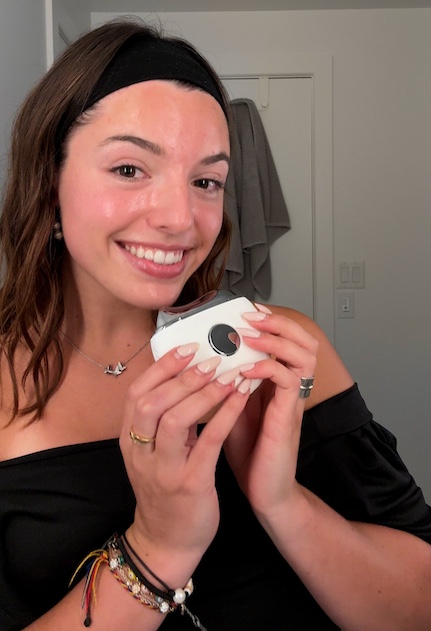 Smiling person holding a small white device in a bathroom.