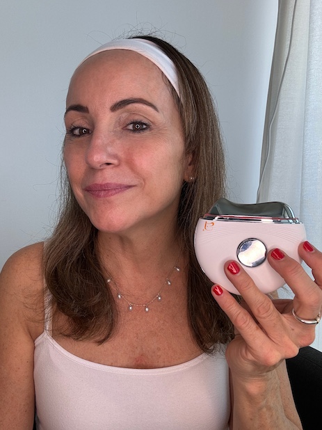Woman holding a facial device, wearing a white headband and necklace.