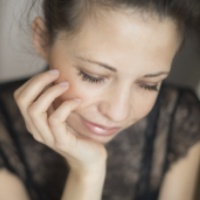 A woman with closed eyes, resting her chin on her hand, wearing a black lace top.