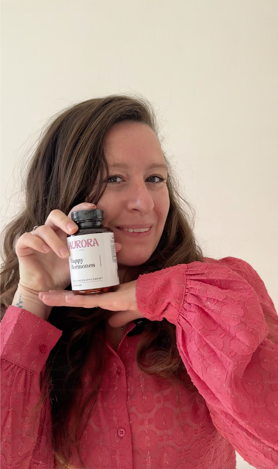 Person in a pink shirt holding a bottle labeled 'Aurora Happy Hormones.'