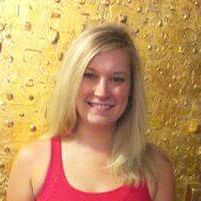 Person with long blonde hair smiling in front of a textured gold background.