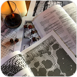 Open books with maps, dice, and a glass of wine on a table.