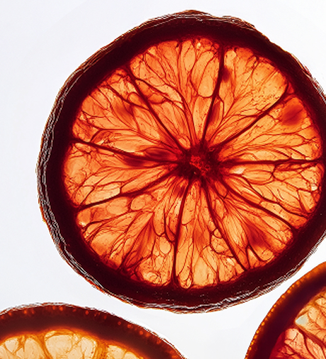 A close-up shot of backlit, translucent slices of blood orange against a white background.