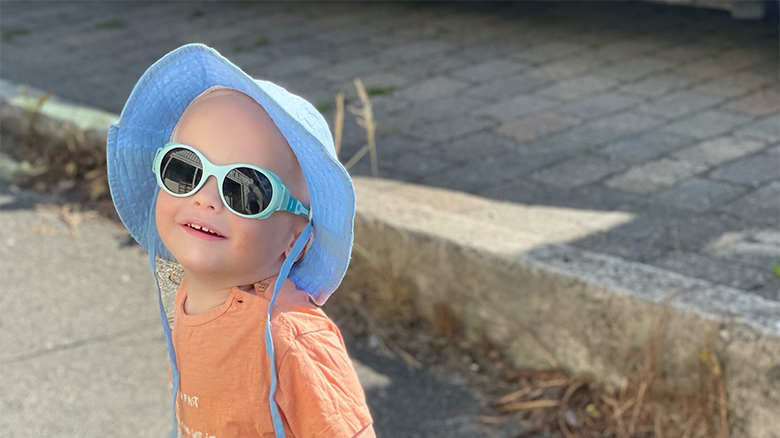 Child wearing sunglasses and a blue hat, smiling outdoors.