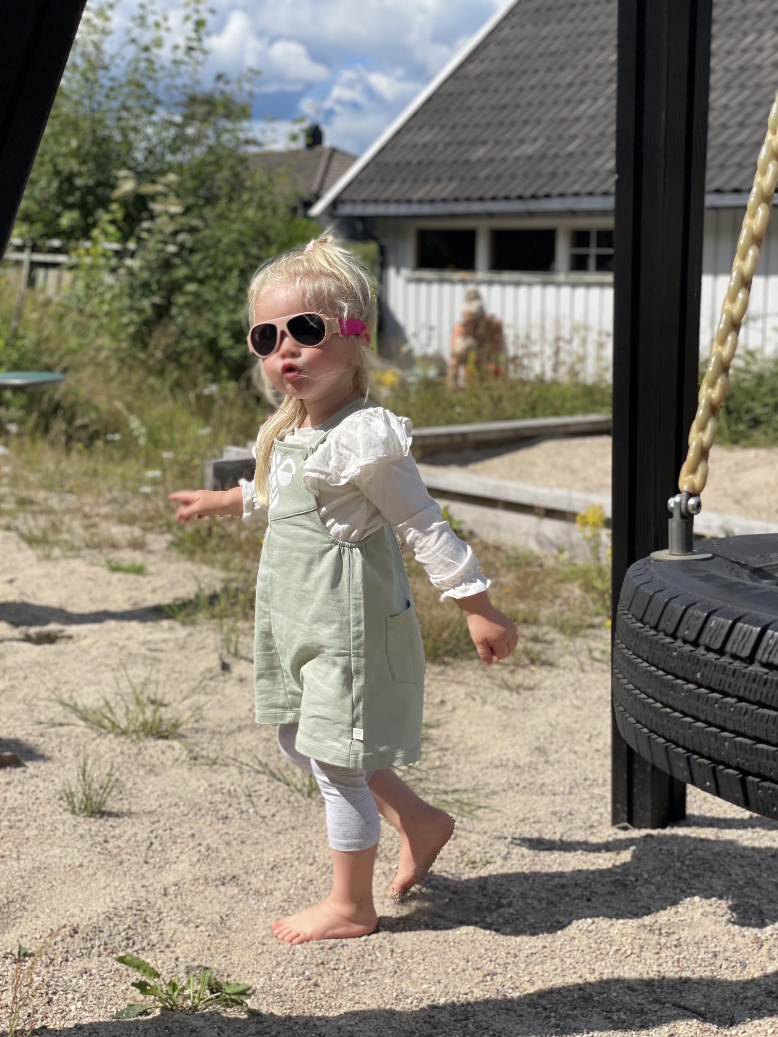 Young child in sunglasses playing outdoors near a swing.