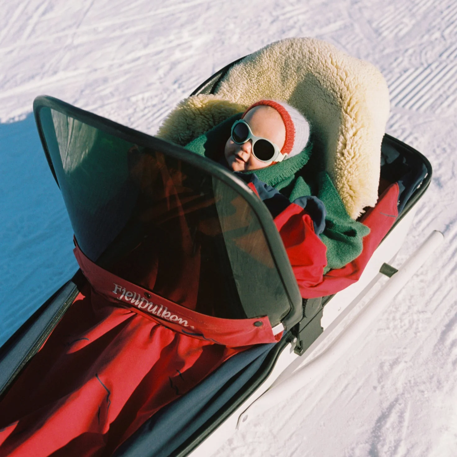 Baby in a sled with sunglasses, surrounded by snow.