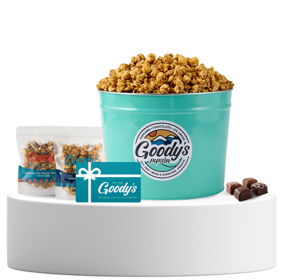 Bucket of popcorn, gift card, two snack bags, and chocolates on a white platform.