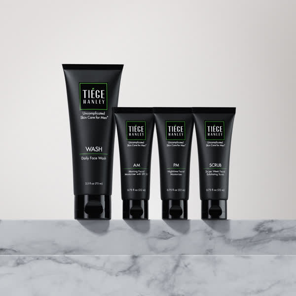 Four black skincare product tubes on a marble surface.