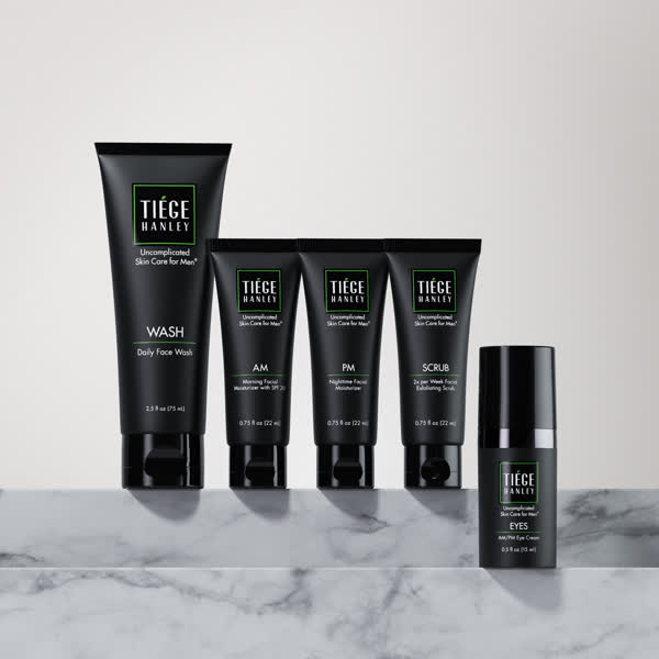 Five black skincare product tubes on a marble surface.