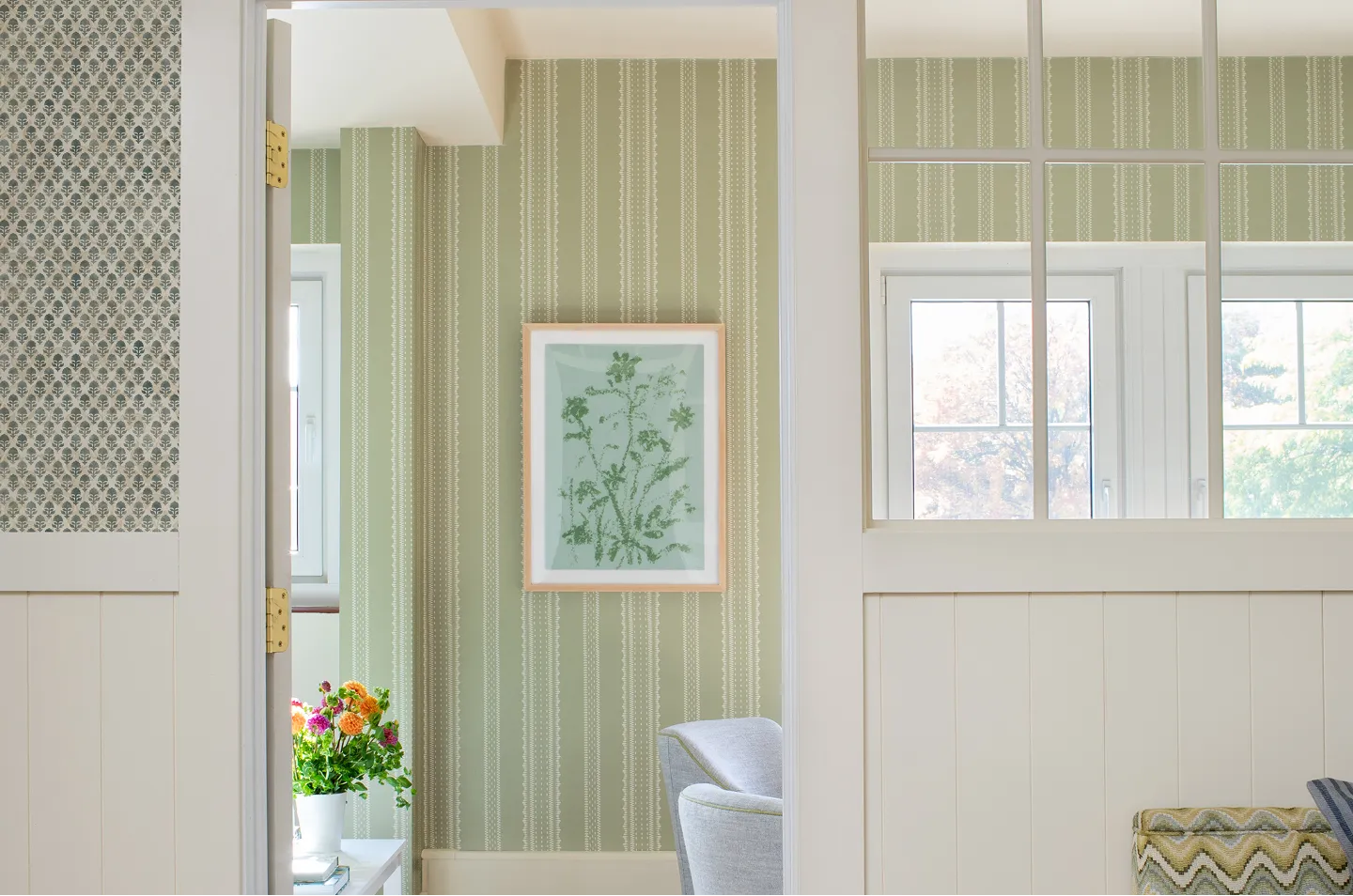 A view through a white doorway into a room with green striped wallpaper and framed botanical art.