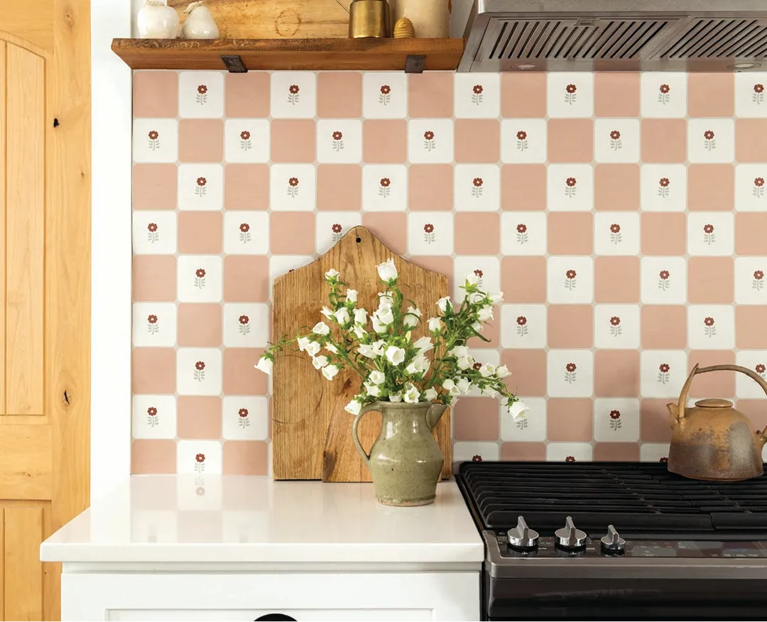 A kitchen backsplash with pink and white floral tiles, a vase of flowers, and a stovetop.