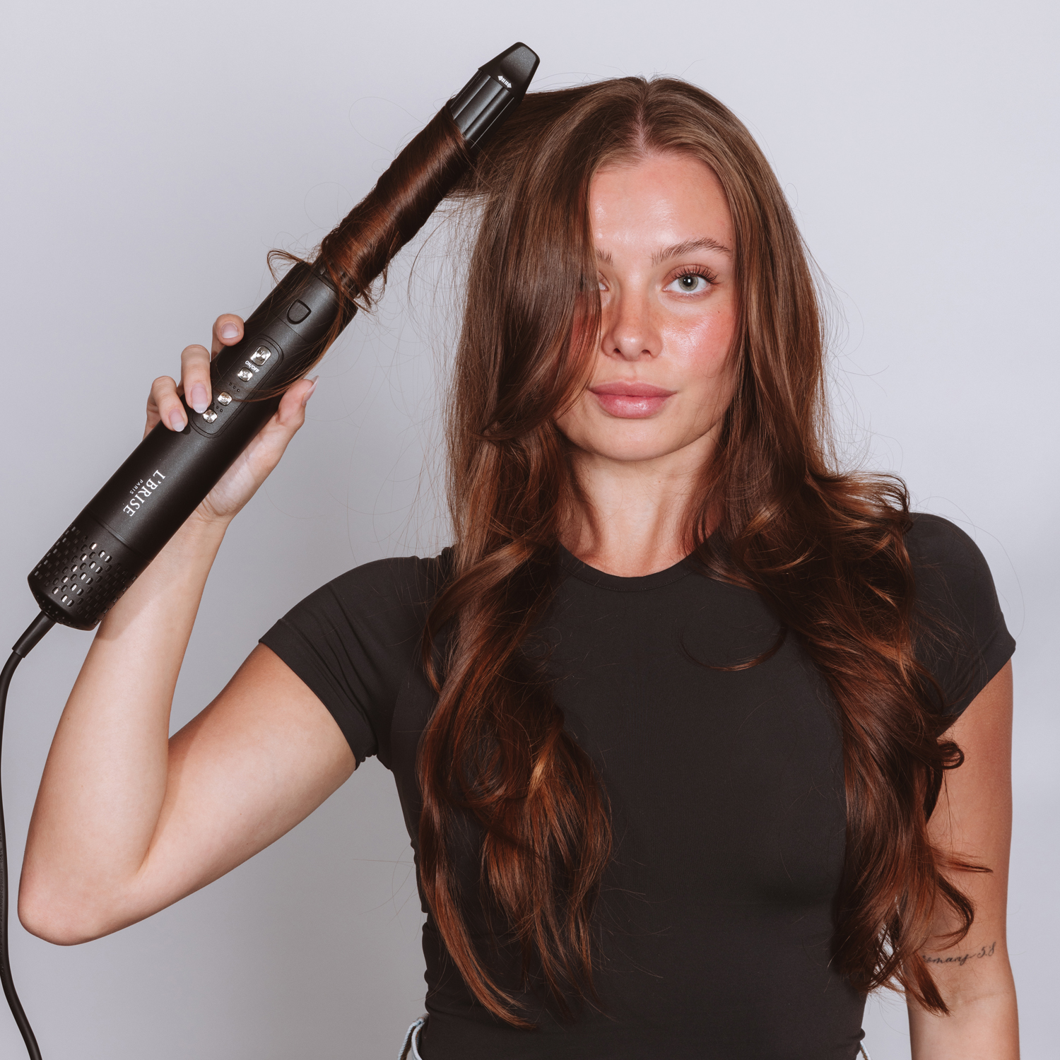 Woman using a hair curling device on long brown hair.