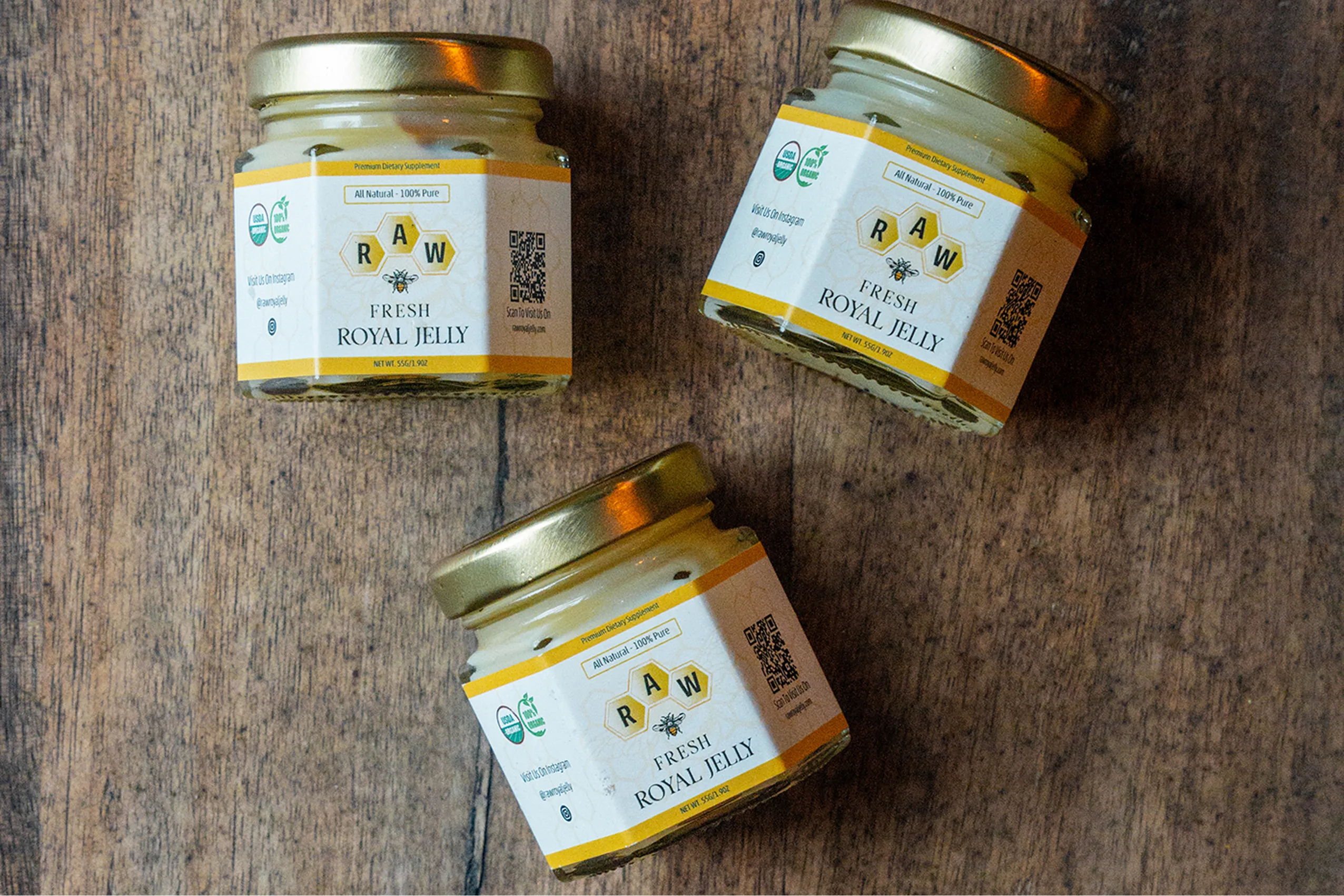 An overhead shot of three jars of raw fresh royal jelly on a wooden surface.