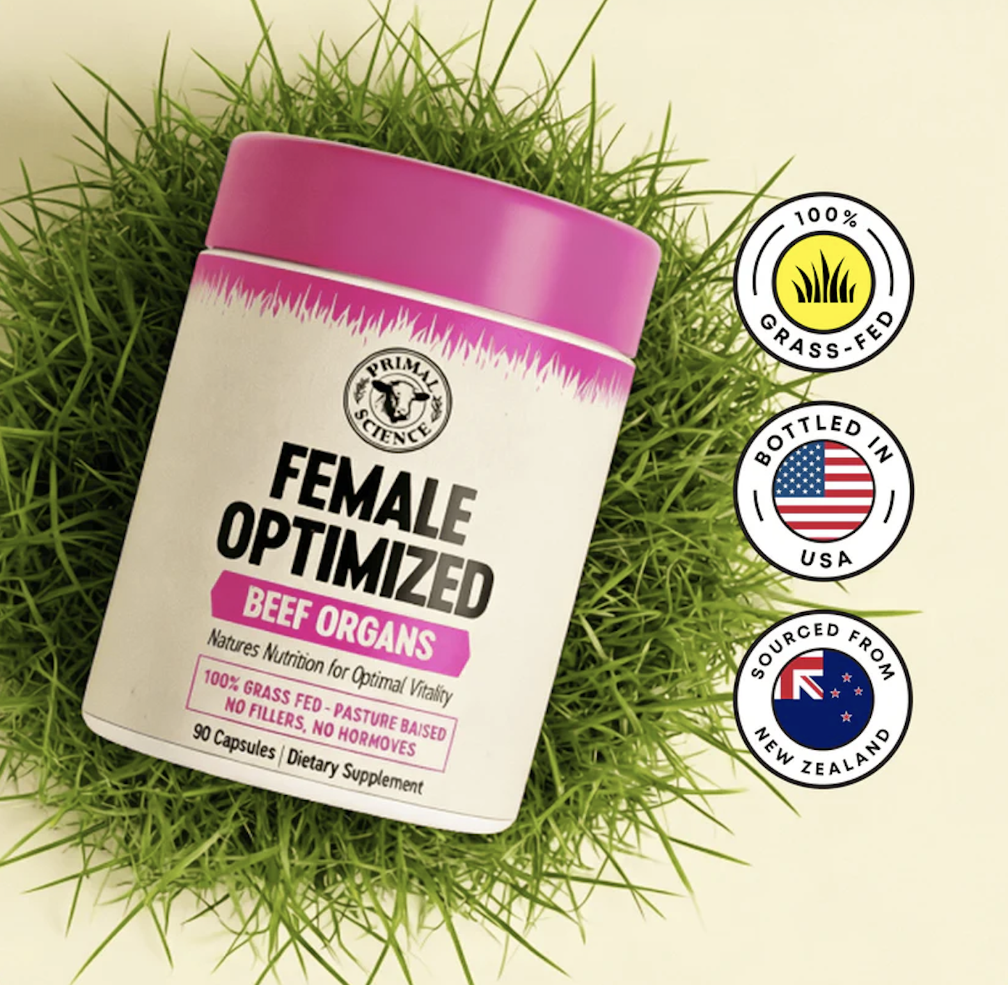A bottle of Primal Science Female Optimized Beef Organs supplements with a pink lid, resting on green grass.
