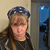 A woman with long brown hair and bangs wears a blue and white patterned bandana indoors.