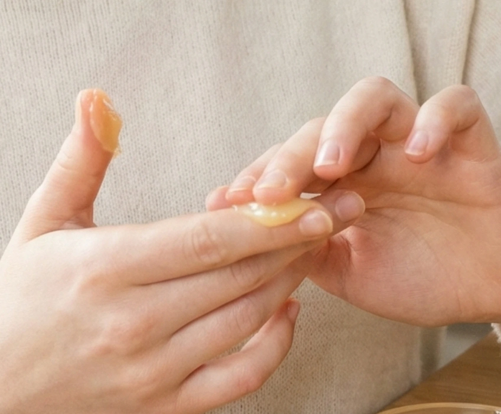 A close-up of a person applying a thick, yellowish balm to their fingers.