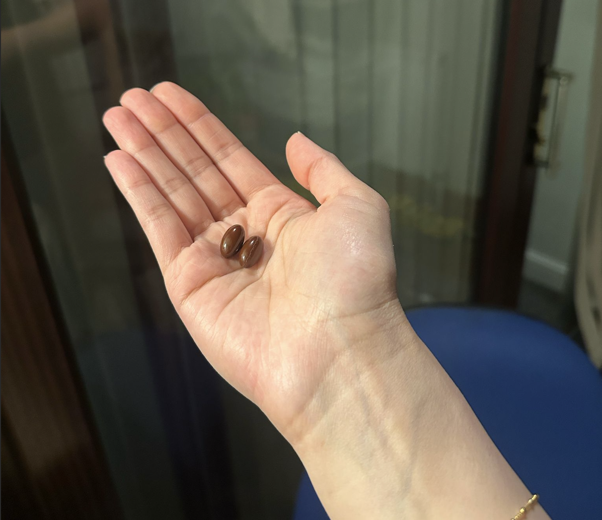 Hand holding two brown oval pills.