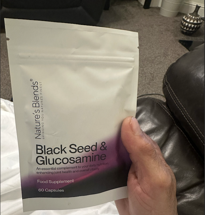 Hand holding a packet of Black Seed & Glucosamine capsules.