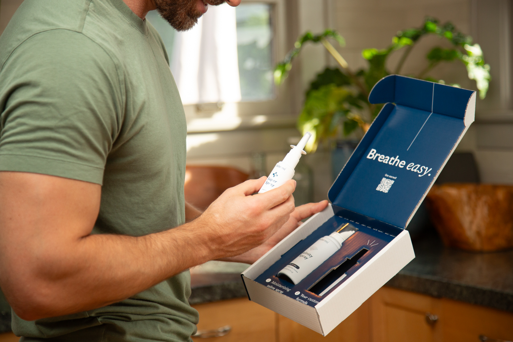 A man in a green shirt holds a nasal spray bottle over an open box containing another bottle.