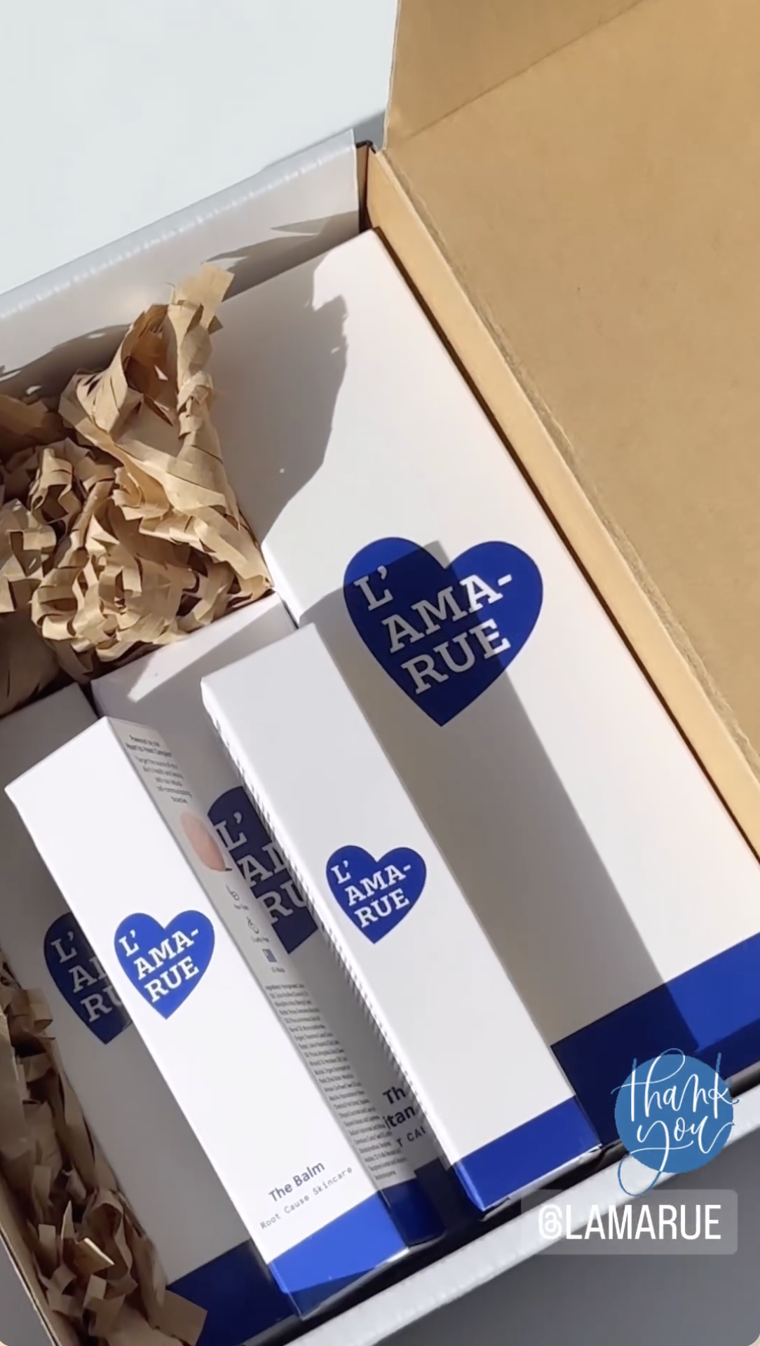 Several L'AMA-RUE skincare products packaged in a cardboard box with brown packing paper.