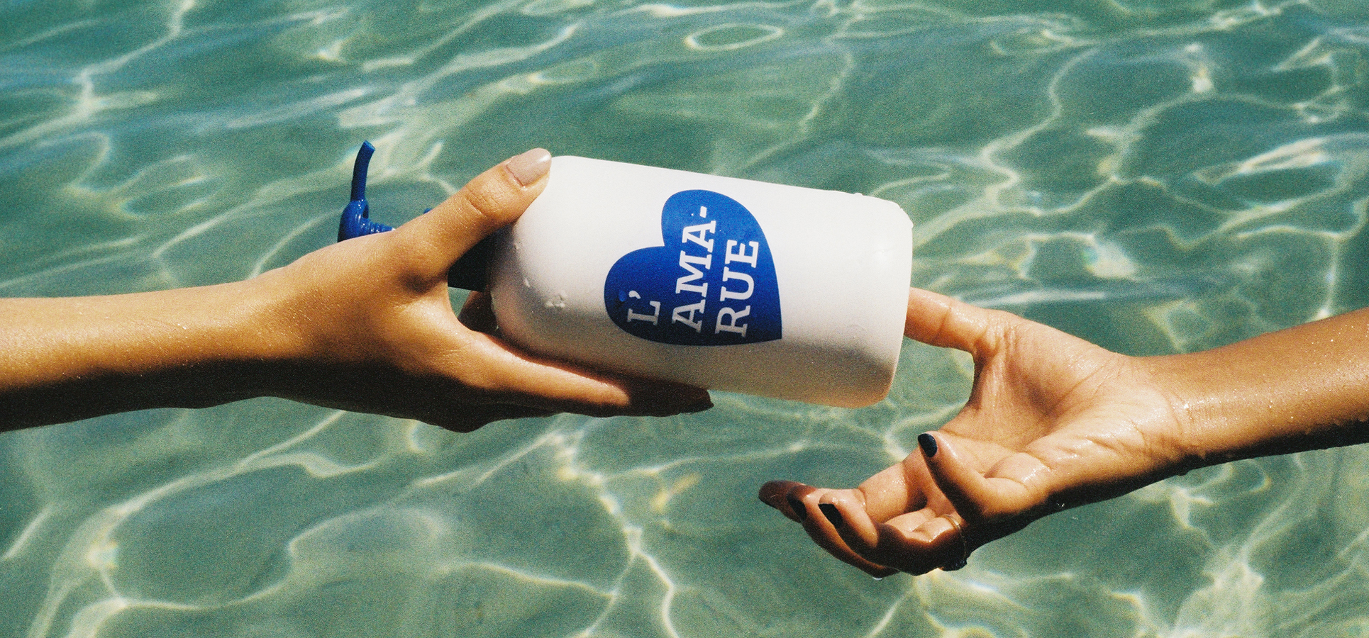 Two hands exchanging a white bottle over clear water.