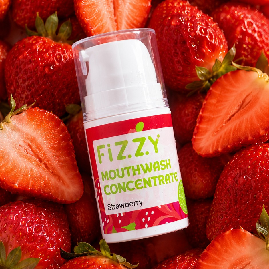 A bottle of Fizzy strawberry mouthwash concentrate resting on a bed of fresh strawberries.
