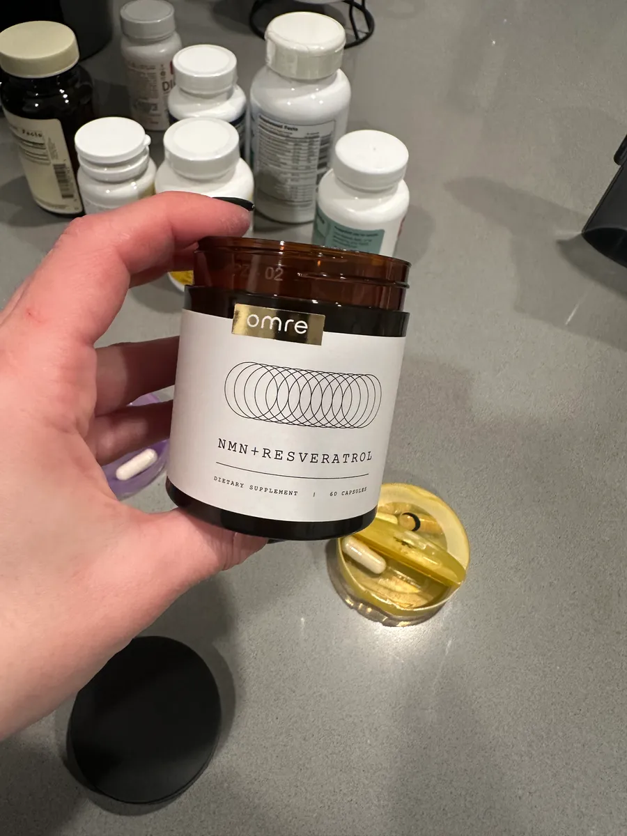 Hand holding a bottle labeled 'NMN+Resveratrol' with other supplement bottles in the background.