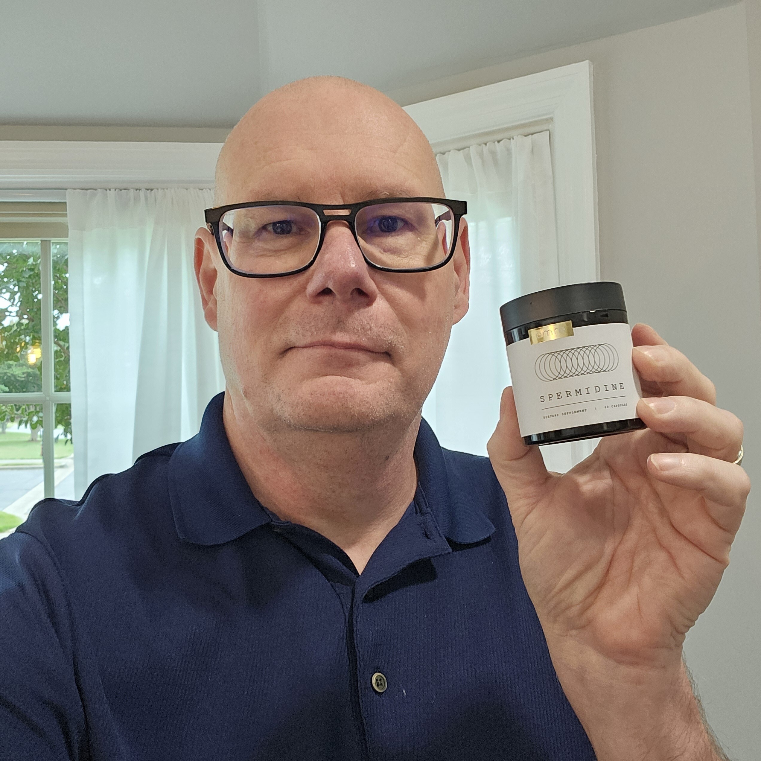Person holding a jar labeled 'Spermidine' in a room with a window.