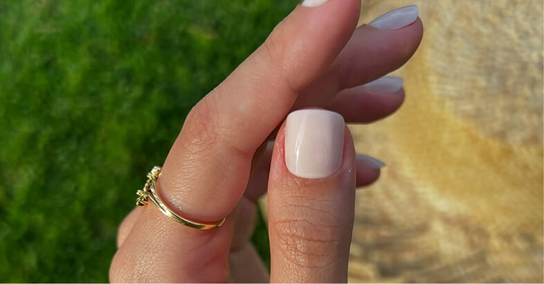 Close-up of fingers with white painted nails and a gold ring.