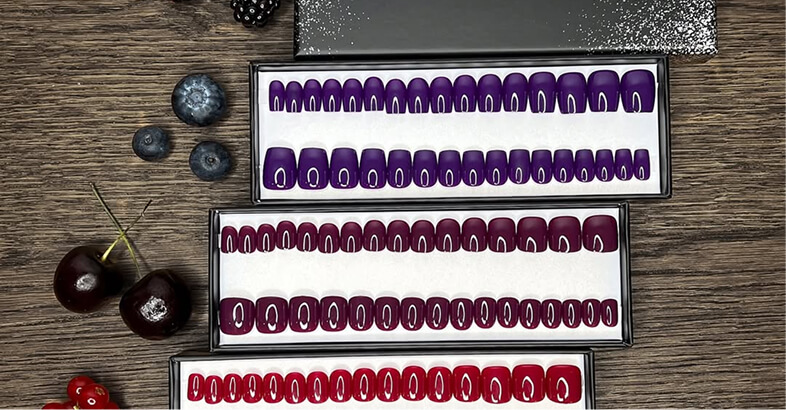 Three trays of colorful artificial nails with berries on a wooden surface.