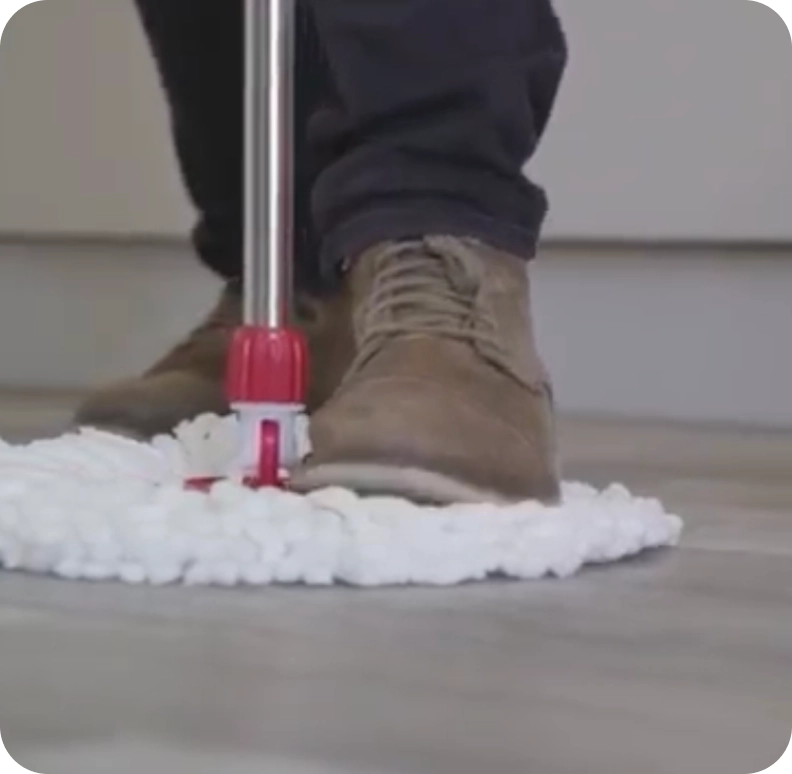 A close-up, low-angle shot of a person using a white string mop to clean a floor.