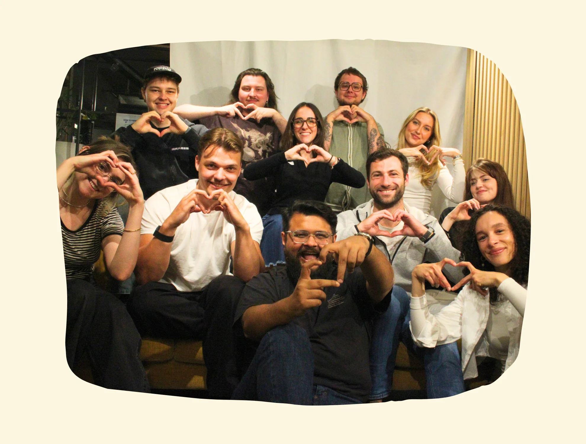 A group of eleven smiling people posing together, many making heart shapes with their hands.