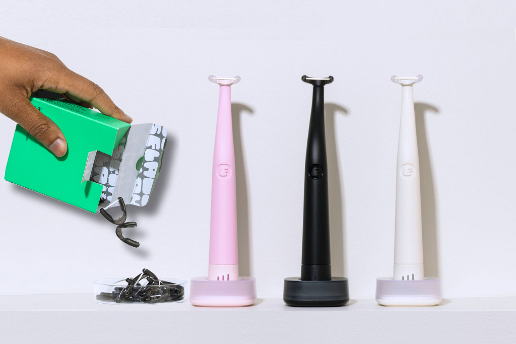 Three electric toothbrushes in pink, black, and white with a hand holding green packaging.