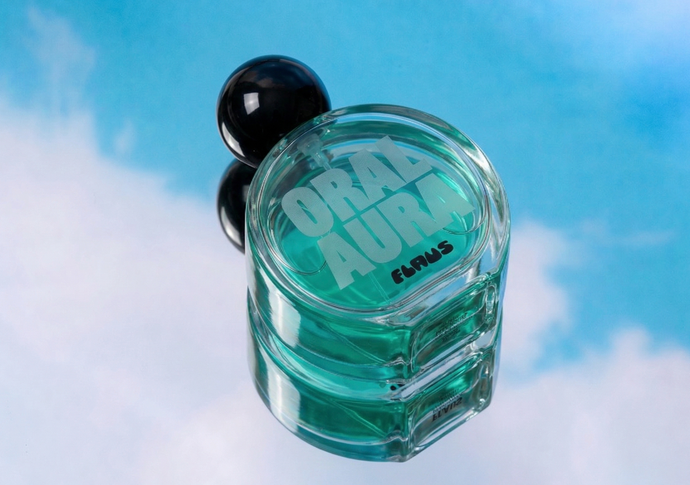 An overhead view of a teal perfume bottle with a round black cap on a mirror reflecting the sky.