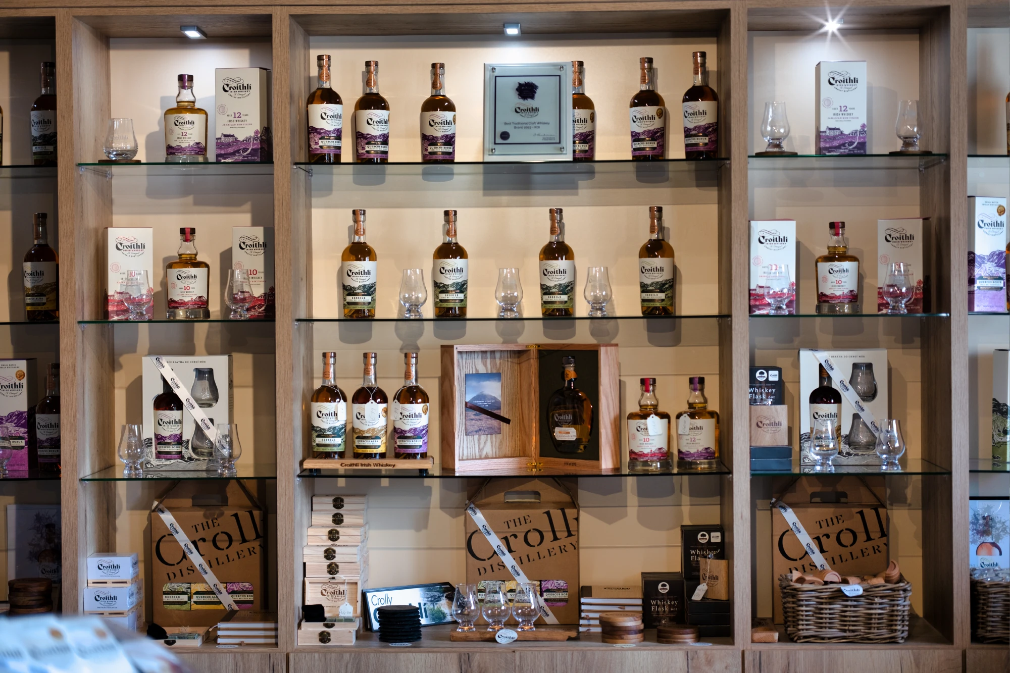 Shelves displaying various whiskey bottles, boxes, and glasses in a distillery setting.
