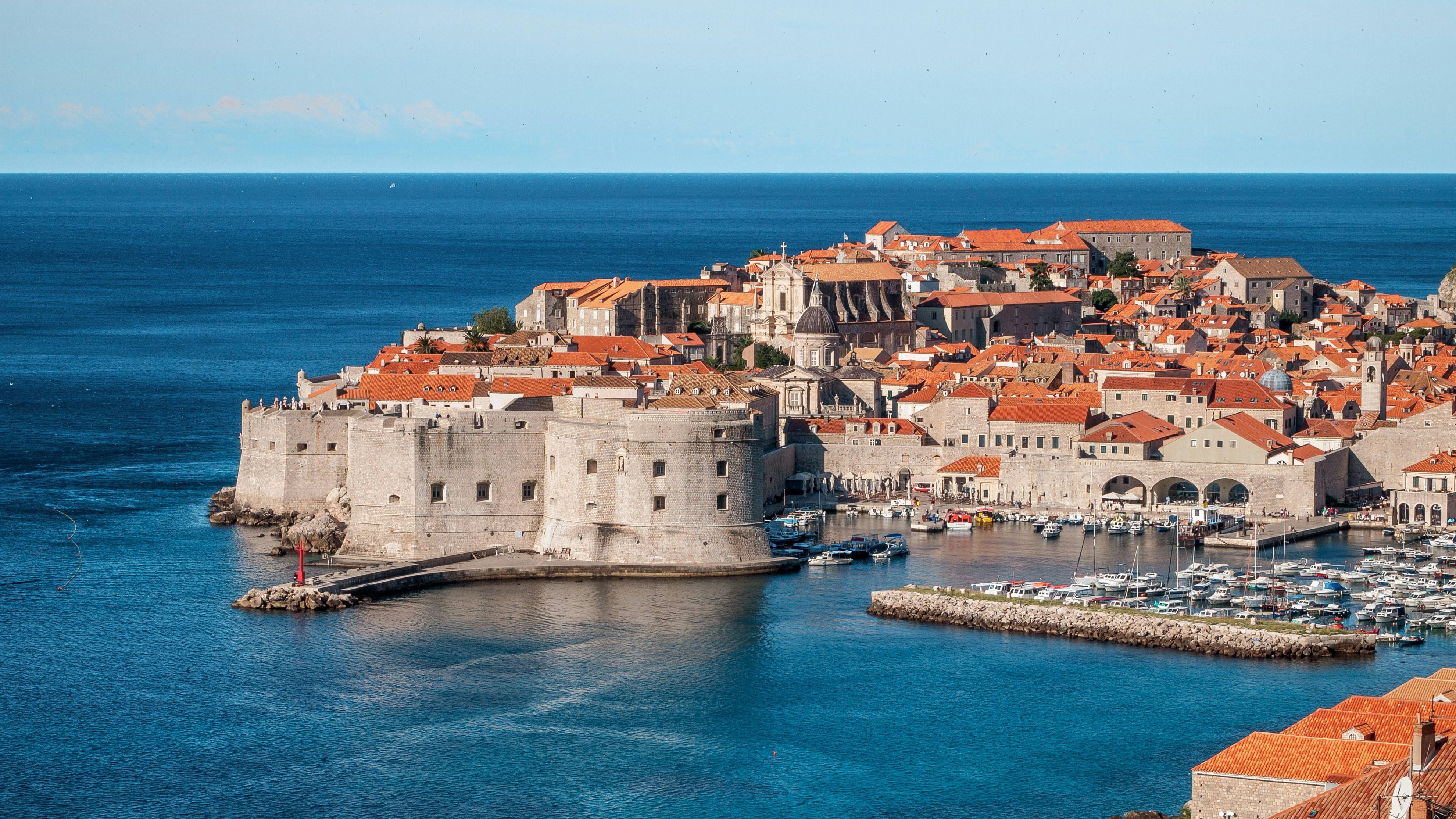 Historic coastal city with stone walls and red-roofed buildings by the sea.