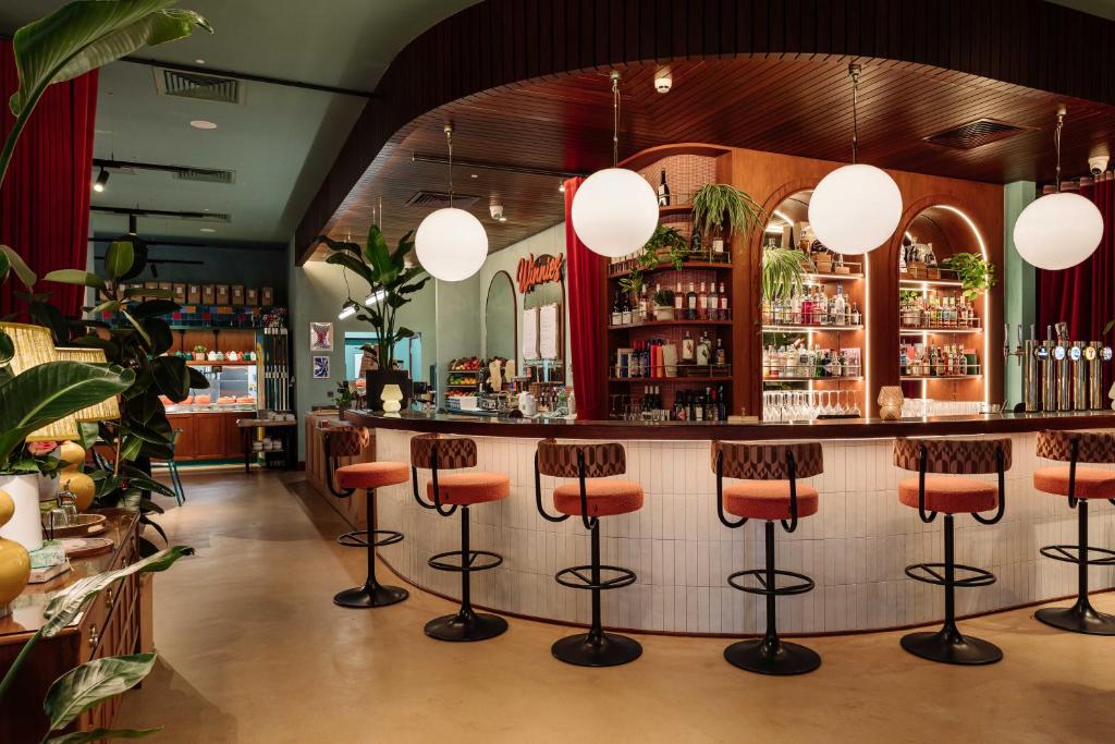 The interior of a retro-style bar with a curved counter, orange stools, and large globe lights.