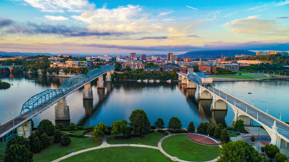 An aerial view of two bridges crossing a river with a city skyline in the background at sunset.