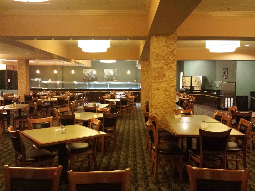 Empty restaurant dining area with wooden tables and chairs, and a buffet counter in the background.