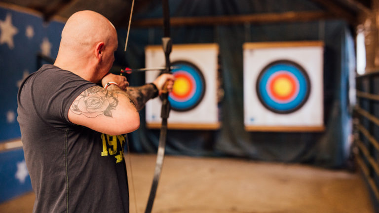 Person aiming a bow at two archery targets indoors.