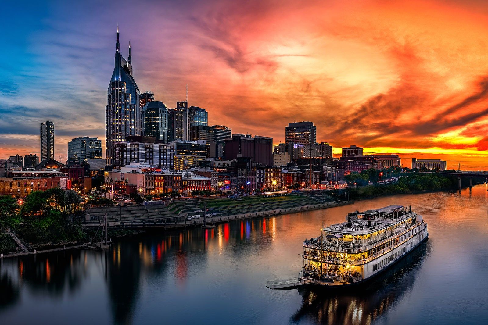 The Nashville skyline with a riverboat on the Cumberland River during a vibrant sunset.