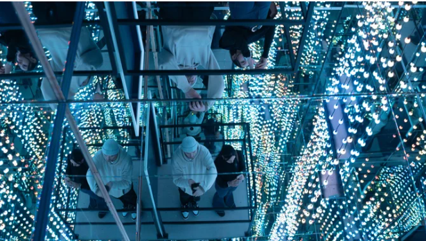 People in mirrored room with blue lights creating infinite reflections.