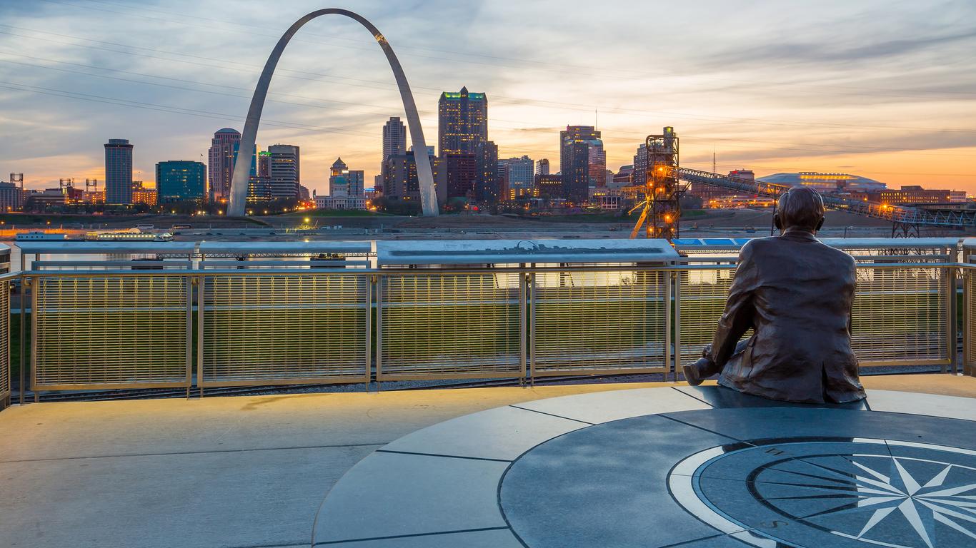 Statue overlooking city skyline with arch at sunset.