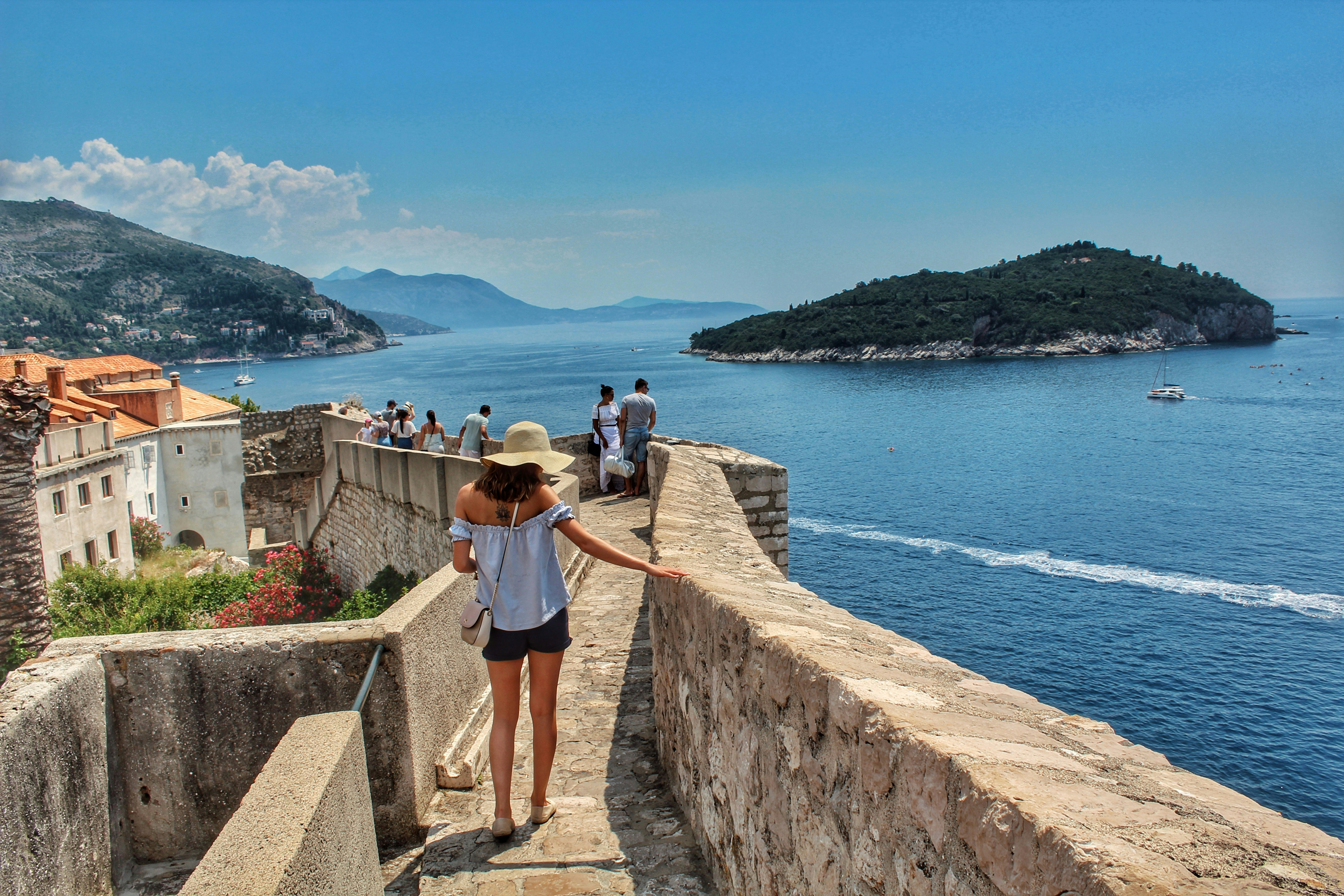 Woman walking on a stone wall overlooking the sea and distant islands.