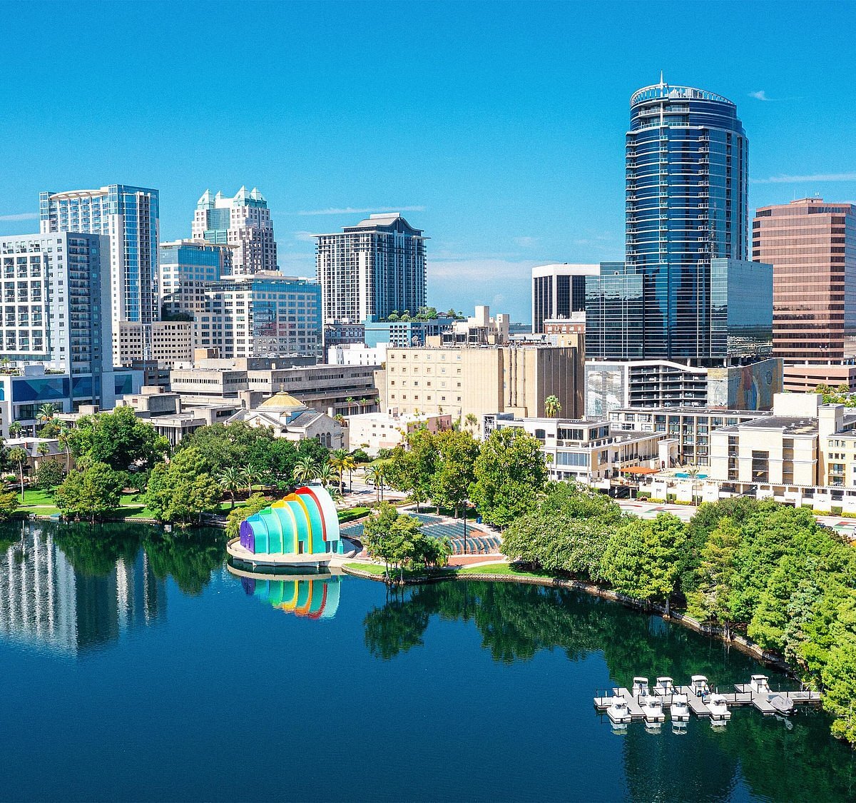 City skyline with tall buildings, a colorful structure, and a lake with boats.
