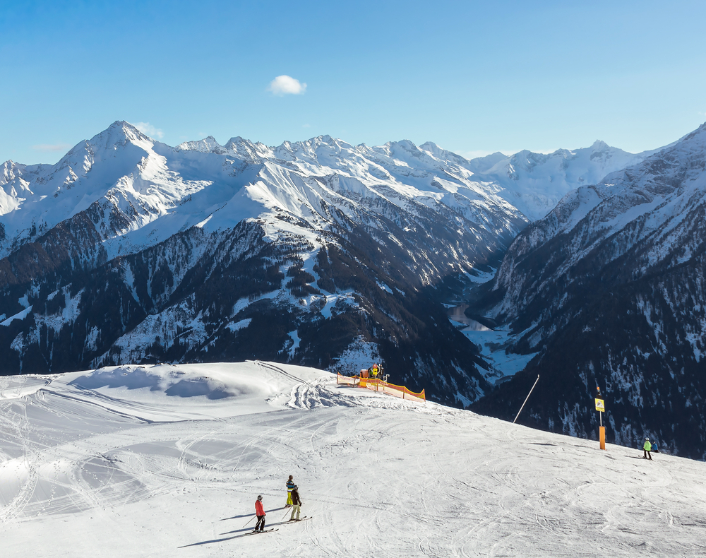 Skiers on a snowy slope overlooking a vast mountain range on a sunny day.