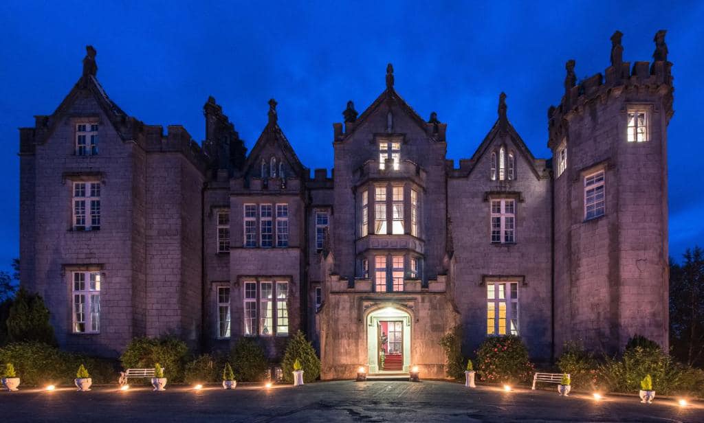 Illuminated stone castle at night with lit pathway and blue sky.