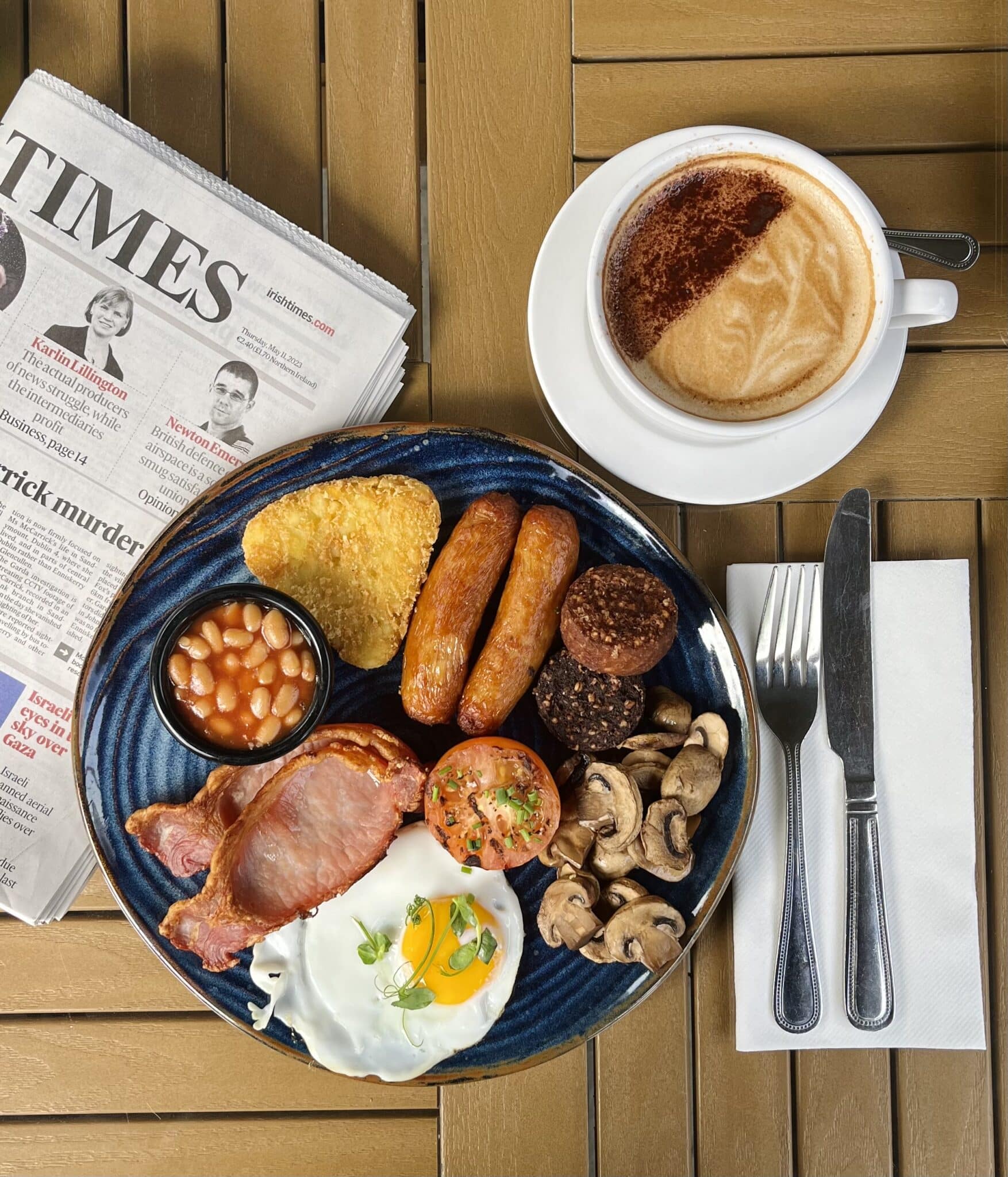 Full English breakfast with coffee and newspaper on a wooden table.