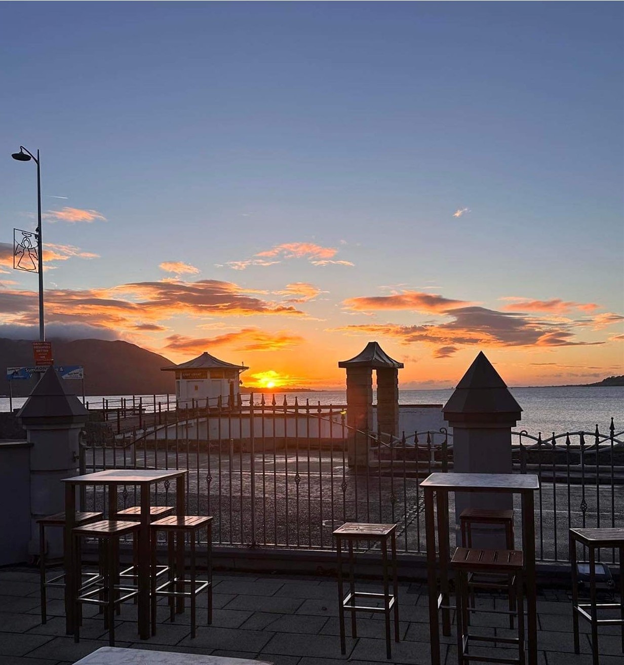 Sunset over a waterfront with tables and chairs in the foreground.