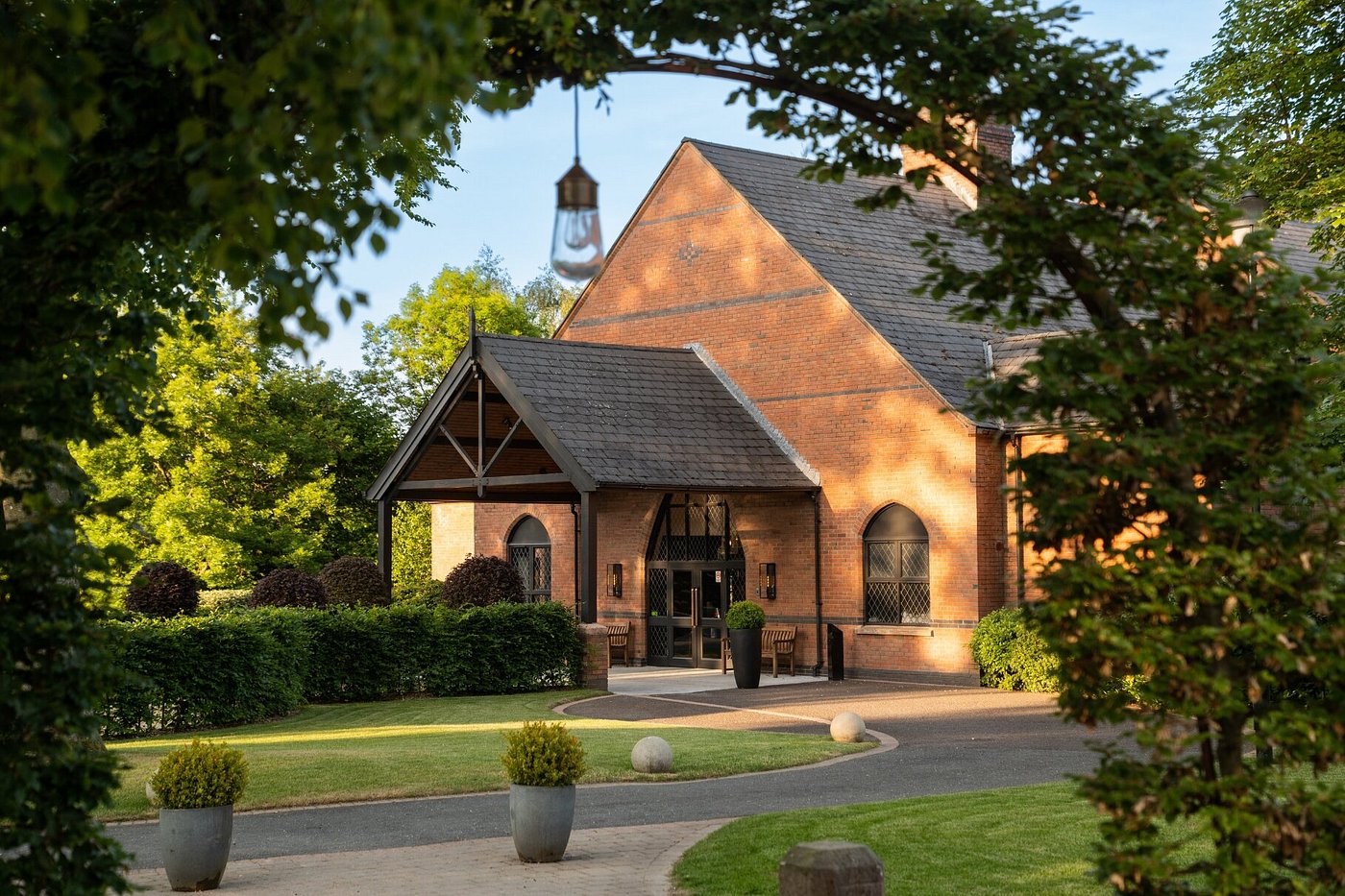 Brick building with arched windows, surrounded by greenery and a paved path.